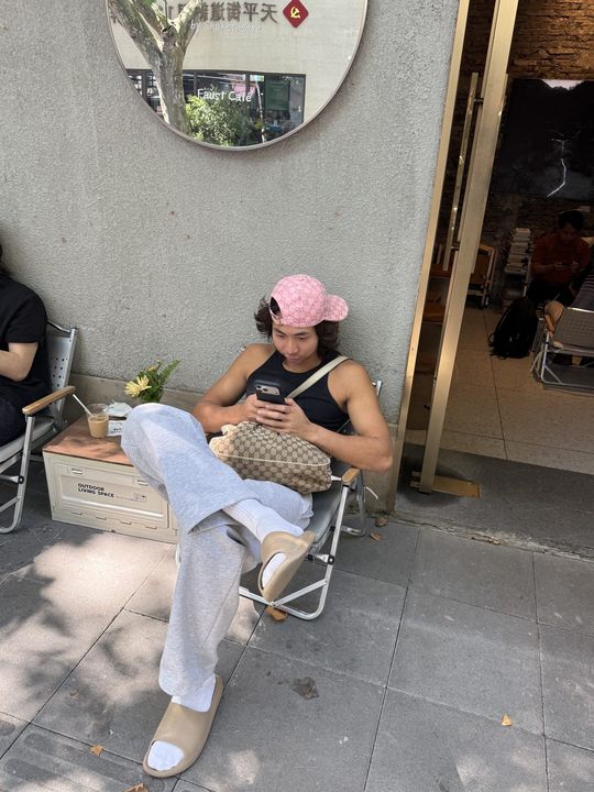 A traveller in a pink cap sitting in a folding chair on a shaded pavement