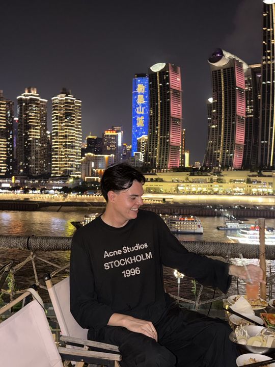 A traveller on the riverbank at night with the Chongqing skyline behind