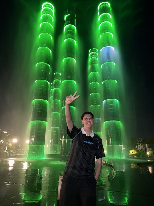 A traveller in front of a fountain lit green at night