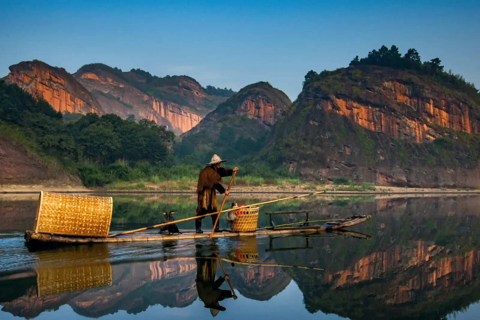 Fisherman guiding a bamboo raft across a calm mountain river