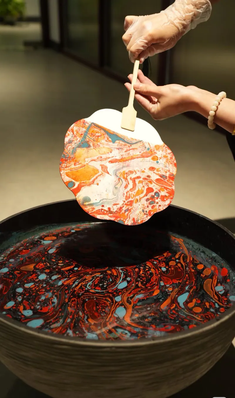 Hands lifting a marbled Chinese fan from a lacquer bath