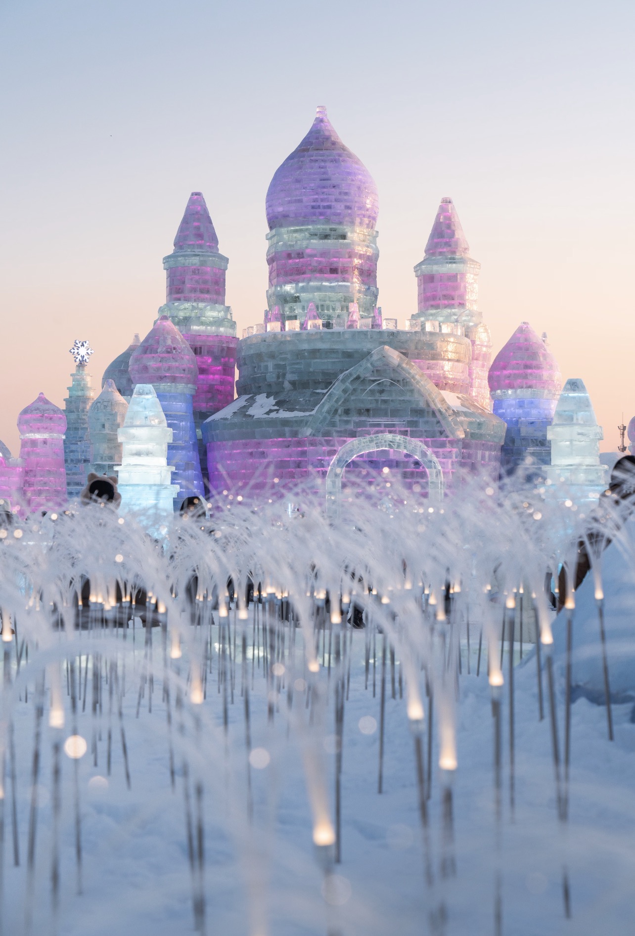 Harbin Ice and Snow World lit at dusk, ice towers on the Songhua River bank